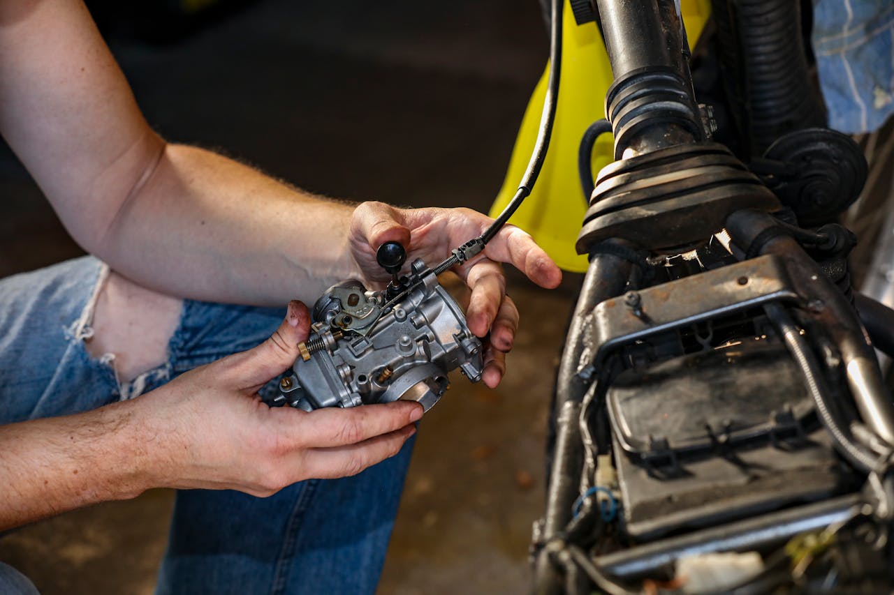 creative-03 Close-up shot of a mechanic's hands repairing a motorcycle carburetor indoors.