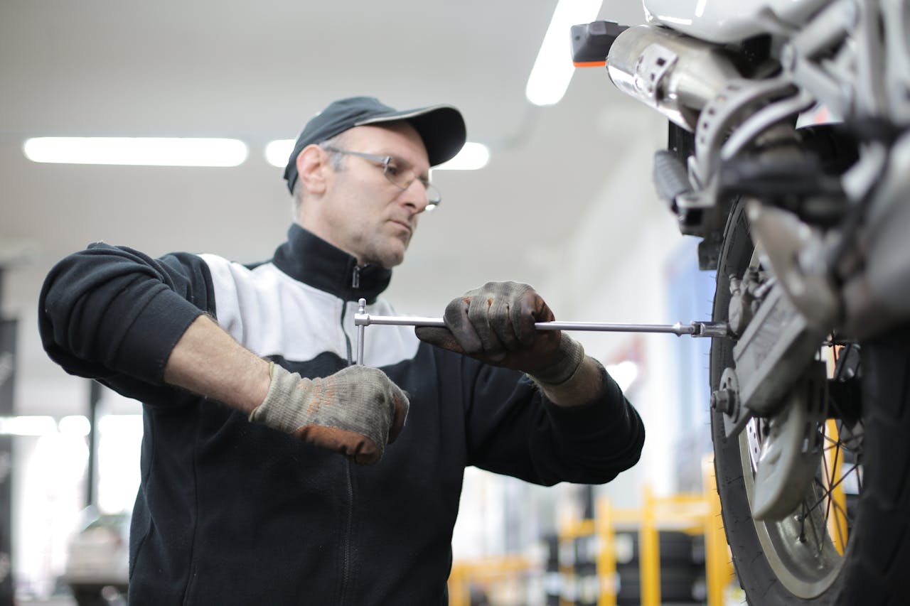 brand-01 Man skillfully fixes a motorcycle tire using a wrench in an indoor workshop setting.