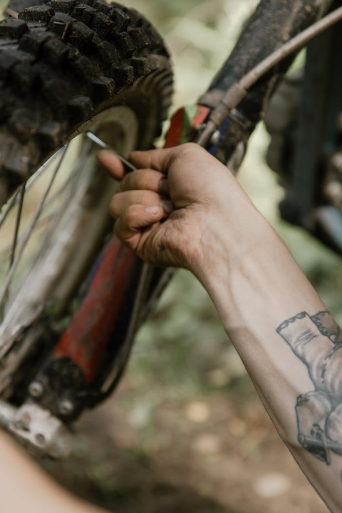 A tattooed hand works on a motorcycle tire in a detailed outdoor close-up.